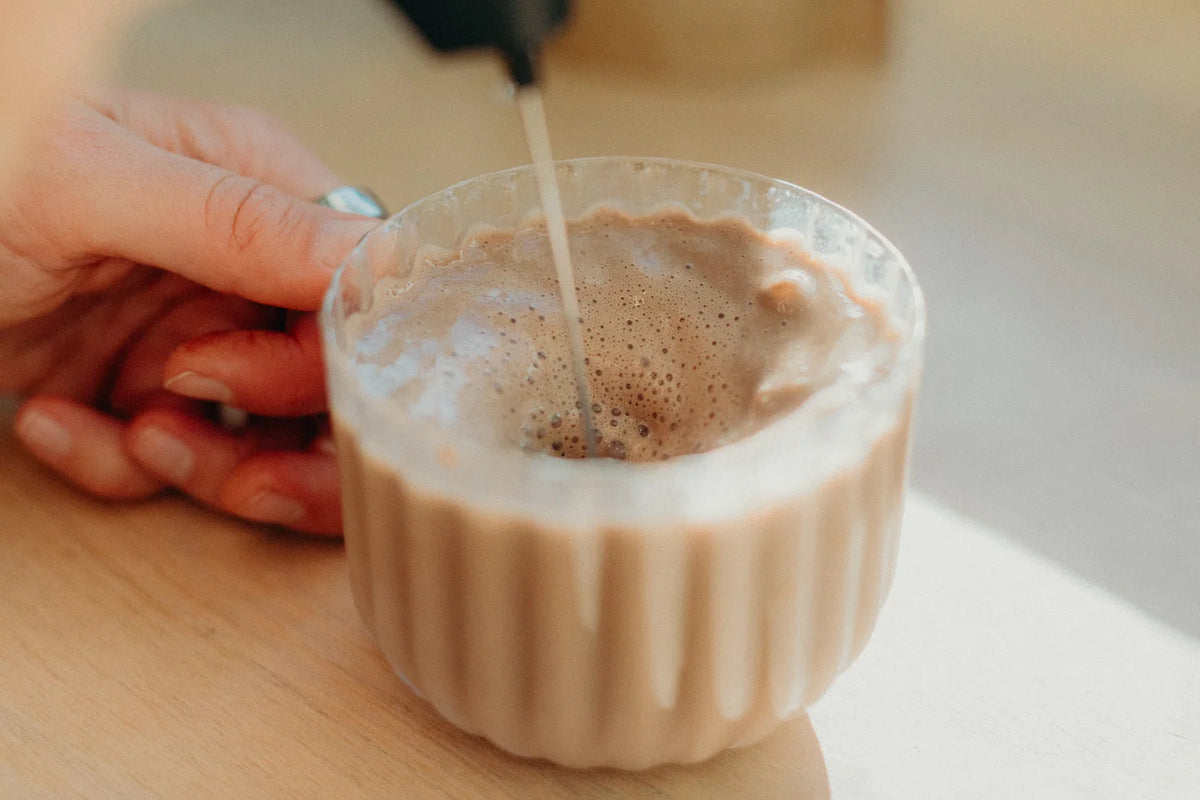 Cacao being frothed in a glass cup on a sunny kitchen table