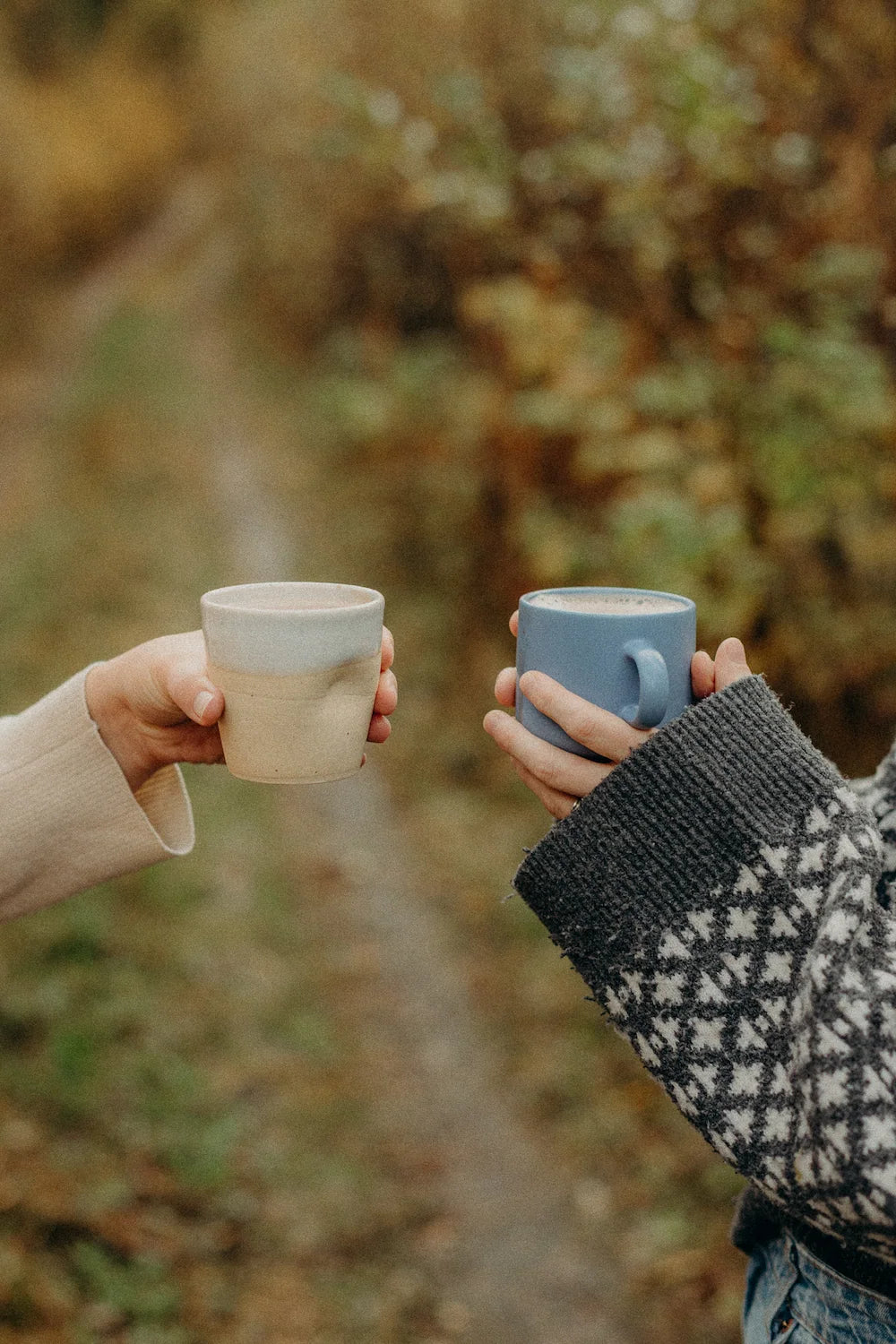 Two cups of cacao raised outdoors in an autumn forest